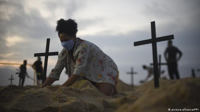 Manifestante simula túmulos na areia em praia do Rio de Janeiro, em protesto contra inação do governo na pandemia