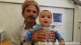 A man in Yemen holds up a malnourished baby (Save the Children/Majed Nadhem)