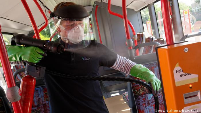 Man in mask and protective gear sprays bus surfaces (picture-alliance/dpa/H. Kaiser)