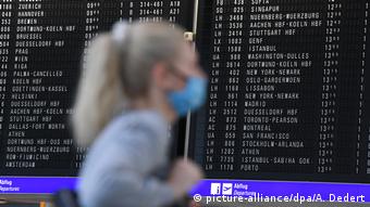 Девушка в маске на фоне табло с расписанием рейсов в аэропрту Франкфурта