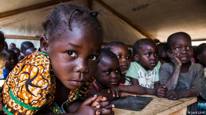 Children gather inside a makeshift classroom under tarpaulins in a sprawling camp (Jack Losh)