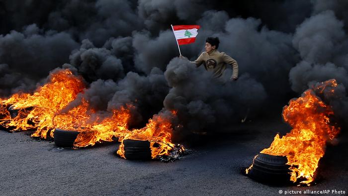 An anti-government protester in Lebanon jumps on blazing tires