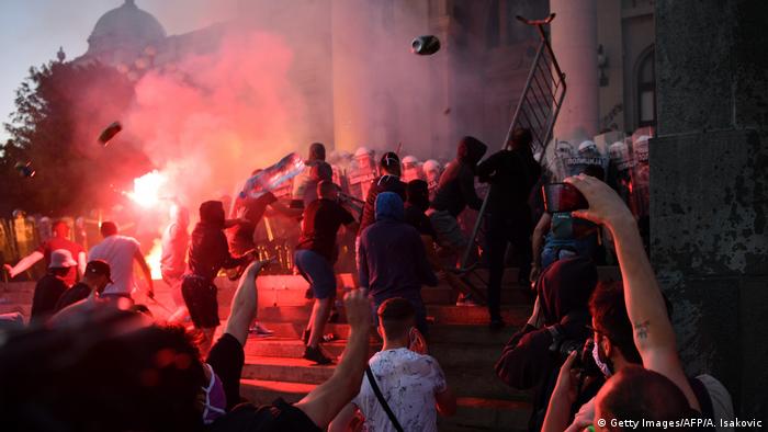 Protesters throw projectiles at riot police outside Serbia's National Assembly building in Belgrade on July 8, 2020, during a demonstration against a weekend curfew announced to combat a resurgence of COVID-19 infections. (Getty Images/AFP/A. Isakovic)