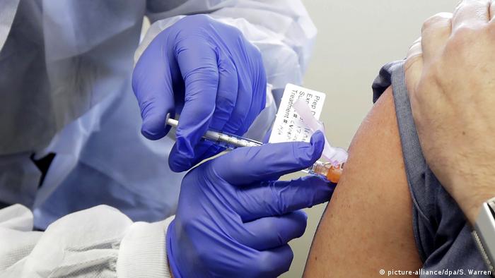 Pessoa com luvas azuis aplica vacina no braço de outra pessoa. Não é possível ver o rosto delas. 