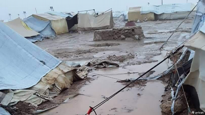 Tents stand on muddy ground covered in puddles