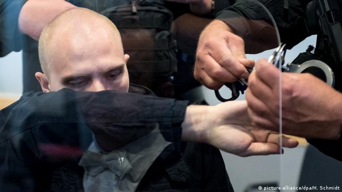 Stephan B., his face covered by his arm, being handcuffed by police