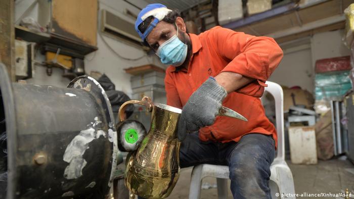 A worker wearing a mask polishes a gold coffee pot into a shine