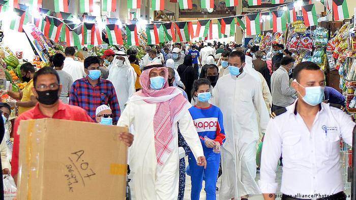 Shoppers walk around in masks under bunting with the flag of Kuwait in a market in Kuwait City