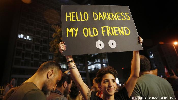 A woman holds a sign above her head which reads 'Hello darkness my old friend'
