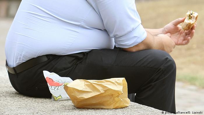 Overweight man eating a hamburger (picture-alliance/D. Lipinski)