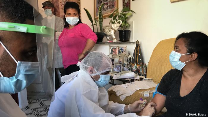 Enfermeiro colhe amostra de sangue de mulher com máscara
