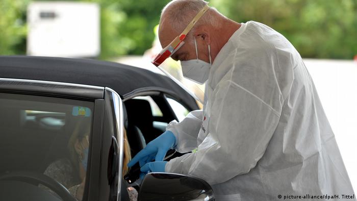 A man in a white protective suit administering a COVID test through an open car window