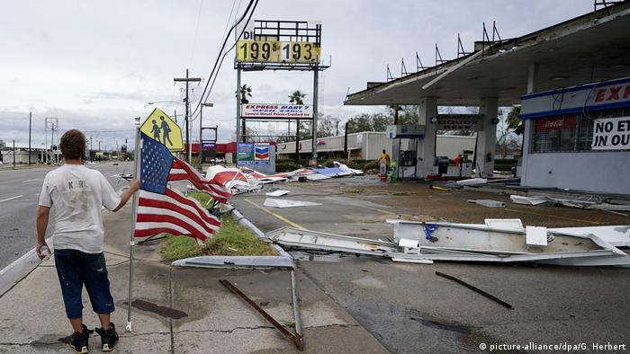 A man holds an American flag in a street surrounded by debris