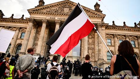Un grupo de personas y una mujer con una bandera roja, blanca y negra, delante del edificio del Reichstag alemán. (29.08.2020).