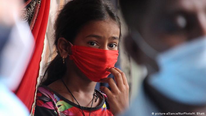 Indien Mumbai | Coronavirus: Mädchen mit Mundschutz beobachtet medizinisches Personal (picture-alliance/NurPhoto/H. Bhatt)