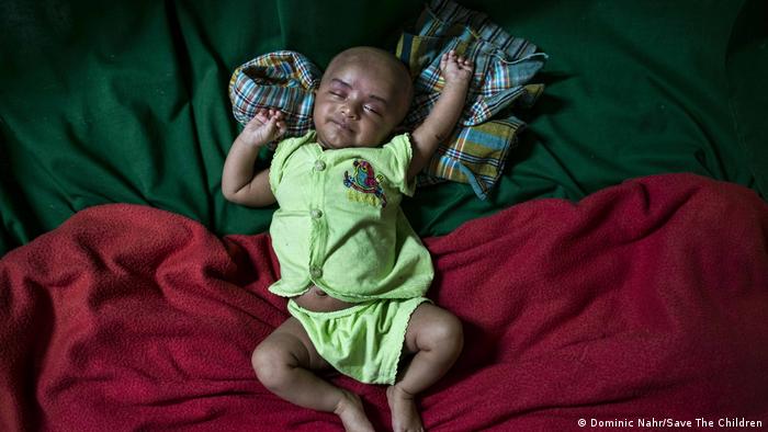 A sleeping baby with arms stretched out, on red and green blankets (Dominic Nahr/Save The Children)