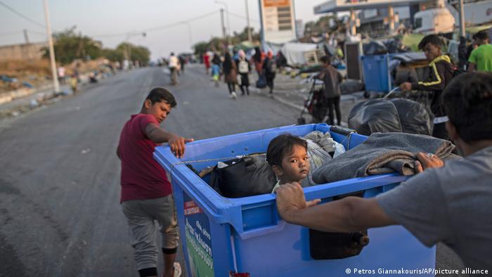 A man and a boy moving a recycling bin with their belongings and a child inside (Petros Giannakouris/AP/picture alliance)