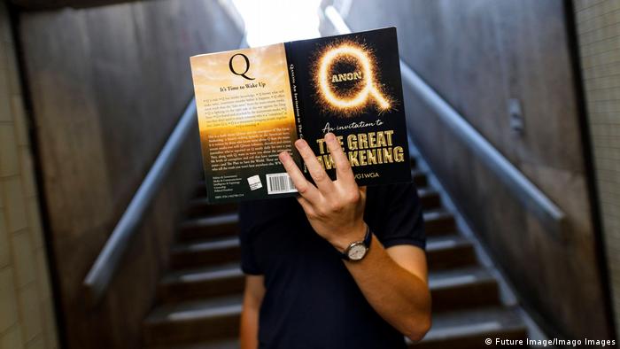 Мужчина в Кельне держит перед своим лицом книгу под названием QAnon: великое пробуждение